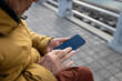 © Devka - An older man sitting on a bench by the lakeside, looking at his mobile phone