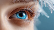 © syhin_stas - Close up of a woman's captivating blue eye showcasing artful winter makeup with shimmering blue eyeshadow and delicate frost like white eyelashes creating an icy beauty look