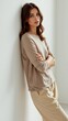 © IgorImageDoc - portrait young woman standing against white wall she wearing beige long sleeved top beige trousers her hair styled loose waves she looking directly camera serious expression her arms crossed front