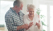 © peopleimages.com - Phone, senior and couple in home with happiness, reading good news or notification. Mobile, elderly man and woman in house for internet, connection or share message for pension increase in retirement