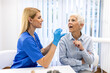 © Graphicroyalty - Professional nurse in blue scrubs using a wooden tongue depressor to examine a senior woman's throat in a clinic. Medical checkup, healthcare and diagnostic concept. Doctor consulting elderly patient.