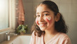 © Rohan Katwe - Young girl laughs while applying face cream in a sunlit bathroom, heart-shaped lotion on her cheek conveying playful self-care, confidence and morning skincare routine at home.