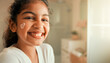 © Rohan Katwe - Young girl laughs while applying face cream in a sunlit bathroom, heart-shaped lotion on her cheek conveying playful self-care, confidence and morning skincare routine at home.