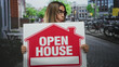 © Krakenimages.com - Woman wearing glasses holding open house sign while puckering lips and peeking over sign on street; invitation playful community.
