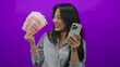 © Krakenimages.com - Chinese woman holding yuan banknotes and smartphone against a purple background, conveying a financial success theme