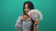 © Krakenimages.com - Young chinese woman in striped blouse holding yuan banknotes against a green background, smiling confidently and pointing to the colorful currency.