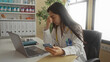 © Krakenimages.com - Woman doctor in clinic using smartphone and laptop, wearing stethoscope, young and chinese, indoors in hospital room, focused on work tasks at organized workplace with files.