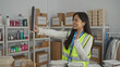 © Krakenimages.com - Young chinese woman in reflective vest conducting a videoconference in a charity's volunteer center surrounded by organized donations and supplies.