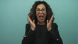 © Krakenimages.com - Woman expressing surprise with hands on cheeks against green wall background with shocked expression wearing black blazer and glasses middle aged hispanic female over isolated scene