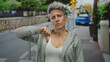 © Krakenimages.com - Caucasian woman with short hair stands on a city street sidewalk and gives a thumbs down gesture in front of a blurred car; disapproval.
