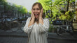 © Krakenimages.com - Woman hands to cheeks smiling on sunlit street in amsterdam canal area wearing striped blouse and watch; surprise travel moment.