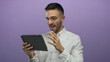 © Krakenimages.com - Young hispanic man expresses triumph while using tablet against vibrant purple background in modern setting showcasing emotions and technology interaction.