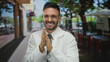 © Krakenimages.com - Hispanic man wearing a white coat and tie standing outdoors on a city street expressing cold with a smile while clapping hands during an urban day.