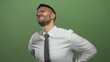 © Krakenimages.com - Young hispanic man in office attire grimacing with back pain against a green background, highlighting workplace discomfort and posture issues.