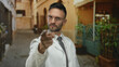 © Krakenimages.com - Hispanic man wearing glasses and a white coat stands pointing with a serious expression on an old city street, suggesting a professional or authoritative persona in an urban setting.