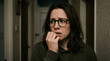 © Serhii - Worried Young Woman with Glasses Biting Her Nails in a Dimly Lit Hallway