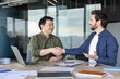 © Liubomir - Two diverse business partners shaking hands, finalizing a deal and showing partnership, collaboration, and trust in a modern corporate meeting setting