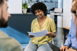 © Xavier Lorenzo - African american businesswoman looking at corporate papers intently, participating in a professional team discussion with diverse colleagues in an office environment