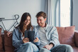© Daniel - Happy couple sitting on a couch, using a tablet together for online shopping or browsing apps, sharing smiles and embracing while managing digital tasks in a relaxed home environment