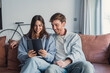 © Daniel - Happy young couple relaxing on cozy couch, using computer tablet together, smiling beautiful woman and man hugging, looking at device screen, watching movie or video, shopping online, browsing apps