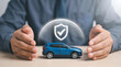 © MZakeer - Car insurance protection concept with hands shielding blue toy SUV and digital shield checkmark icon, vehicle safety coverage, auto insurance approval and protection service on wooden desk