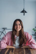 © Daniel - Cheerful young business professional woman in pink casual shirt sitting at desk relaxing indoor, looking at window away, smiling, thinking. Happy pensive female manager, entrepreneur portrait 