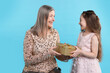© New Africa - Little girl greeting her grandmother with gift on light blue background