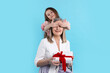 © New Africa - Little girl surprising her grandmother with gift on light blue background