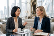 © Meow Creations - Two diverse female executives discussing strategy in office lounge