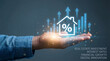 © shahabudin - Human hand holds a glowing digital house icon with a percentage sign and rising blue bar graphs representing real estate investment and financial grow