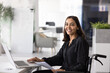 © fizkes - Positive Middle Eastern female worker in wheelchair working in company with policy of inclusion, using laptop computer for analyzing paper reports, sitting at workplace, looking away, smiling