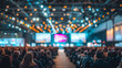 © Dionisia - Audience at large conference event with blurred stage and colorful lights, crowd attending seminar or live presentation, convention hall atmosphere, corporate gathering and networking scene