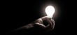© Olha - The light bulb held in a hand glowing against a dark minimalist background