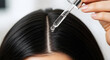 © Unique design - Close up of dropper applying clear liquid serum to dark hair scalp treatment