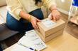 © AntonioDiaz - Closeup of a woman handling shipping labels and packages for an e-commerce side hustle, managing online business orders from home