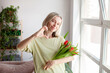 © Tatyana Gladskih - Adult woman with bouquet of tulips at home, woman was given flowers, woman shows a heart sign in gratitude