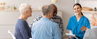 © Prostock-studio - A nurse leads a discussion with a group of seniors in a care facility. The nurse is smiling and holding a clipboard as the seniors engage in conversation.