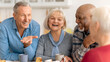 © Prostock-studio - Four friends gather around a table in a kitchen, sharing laughter and stories while enjoying coffee and cake. The mood is friendly and lively as they connect and reminisce.
