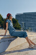 © SHOTPRIME STUDIO - relaxed young woman sitting outdoors in casual denim outfit wearing sunglasses and red bandana enjoying sunny day near urban architecture