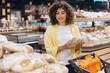 © anatoliycherkas - Young woman shopping for fresh bread in a modern supermarket, choosing items from the bakery section on daily errands