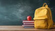© Ilya - Yellow backpack and books on wooden desk in front of classroom chalkboard, student preparation concept, education lifestyle scene, back to school season.