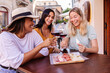 © Xavier Lorenzo - Young multiracial women friends drinking wine at outdoor cafe table. Happy female friends enjoying conversation and wine in a charming European street. Friendship and lifestyle concept.