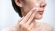 © BJ Day Stock - Close-up of asian female applying white moisturizing cream to their face. Natural skin texture with freckles on a white background. Ideal for skincare and beauty routines.