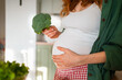 © wifesun - Pregnant woman embracing her belly while holding a fresh head of broccoli, symbolizing conscious and healthy nutrition choices for both mother and child during pregnancy