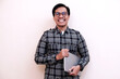 © Nurma - Man smiles warmly while holding a laptop. He wears glasses and a casual shirt. Background is plain, bright, and neutral. Ideal for tech, education, or remote work visuals
