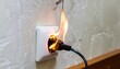 © TransPicHub - A power plug connected to a wall socket is overheating and catching fire, posing a serious electrical hazard.