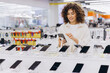 © anatoliycherkas - Woman shopping for a new smartphone, examining models on display in an electronics retail store