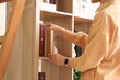 © Pixel-Shot - Young woman taking book from bookshelf in cozy home library, closeup