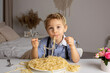 © Tomsickova - Cute preschool child, blond boy, eating spaghetti at home, making a mess everywhere