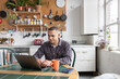 © ReeldealHD images - Young man paying bills online in the kitchen